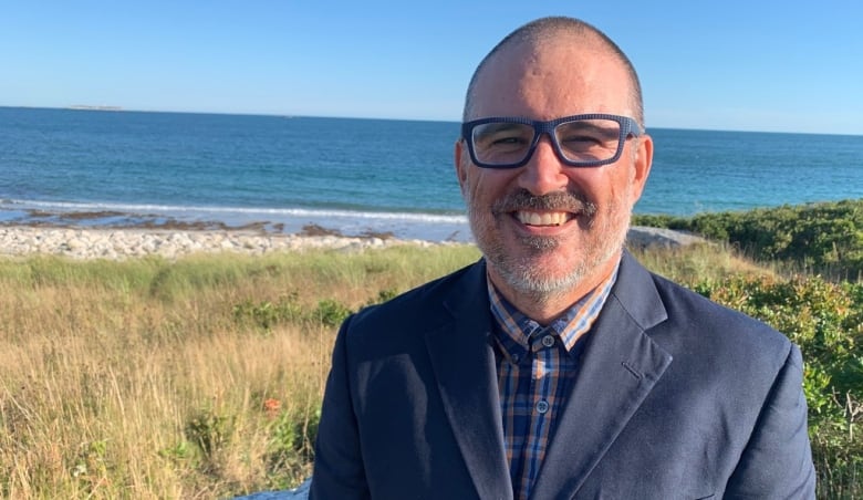 A man smiles for a headshot near a beach.