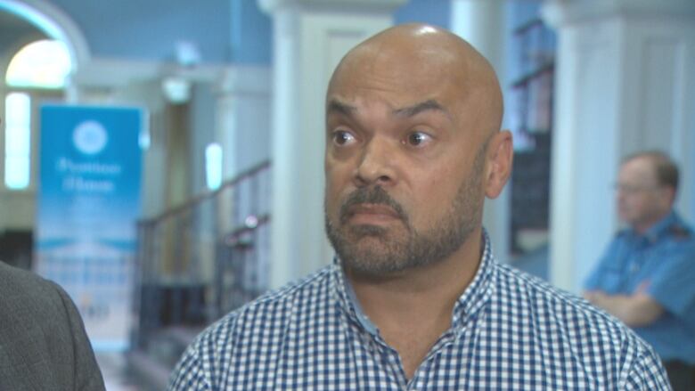 A bald African Nova Scotian man is seen wearing a blue and white gingham button down shirt.