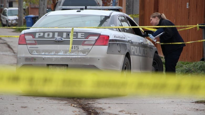 A police car is parked in an alley and surrounded by yellow police tape