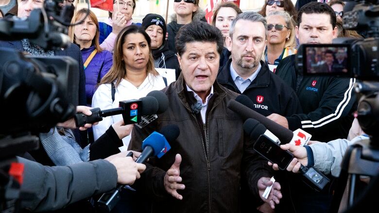 A man surrounded by a crowd and microphones.