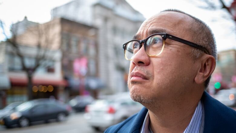 Ken Lum is a middle-aged Asian man. The image is a side profile picture of his face as he stares happily up into sunshine while standing in the streets of Vancouver.