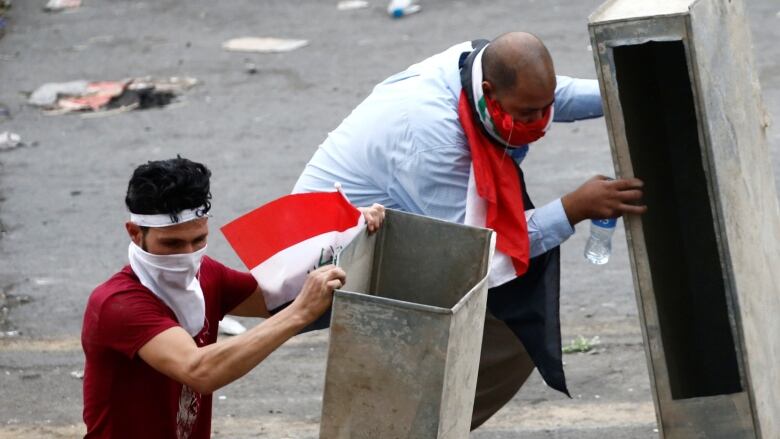 Demonstrators take cover during a protest in Baghdad. They have bandana-like masks and are carrying flags.