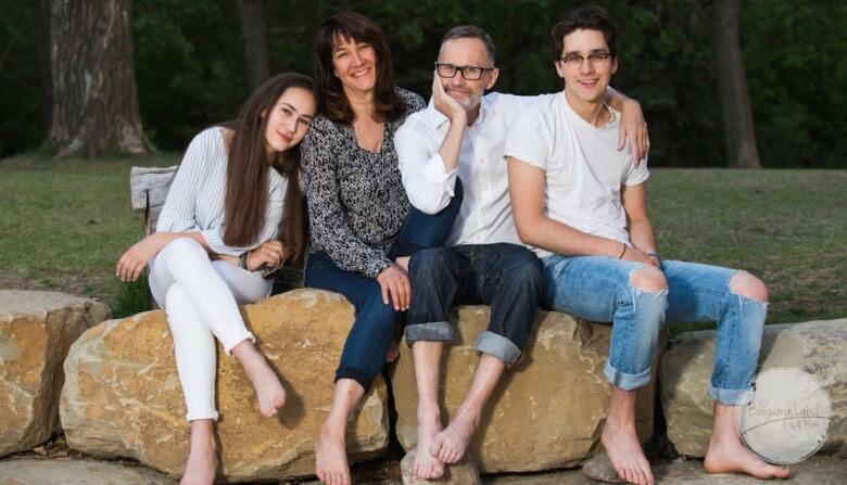 Jim Button, his wife, son and daughter sit on a line of boulders in a park setting.