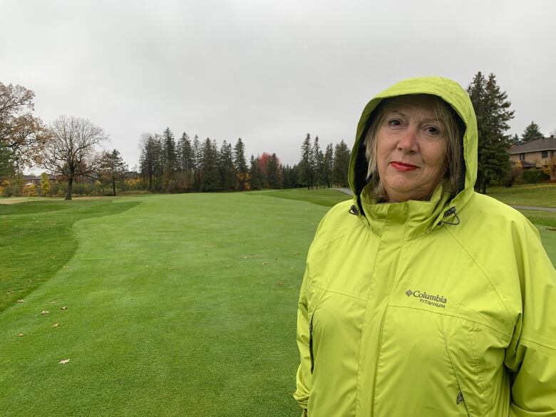 A woman in a bright green rainjacket stands on a golf course