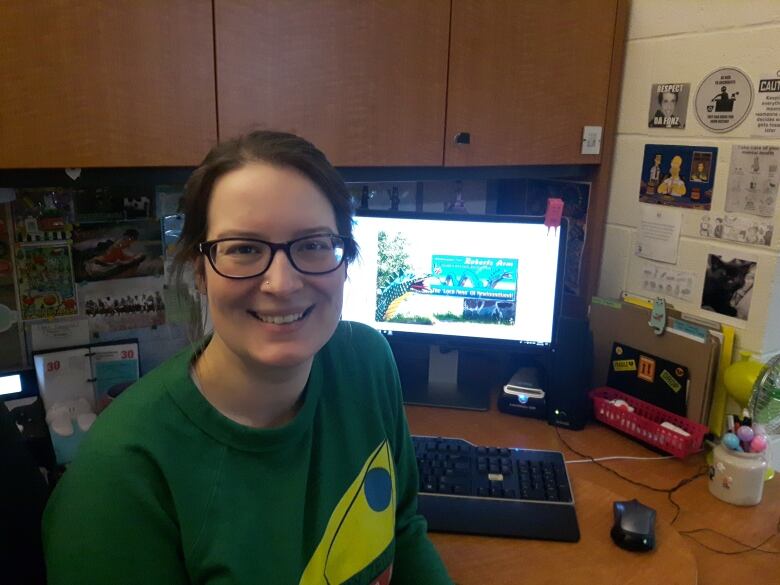 A smiling woman sits at her computer desk.