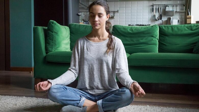 A woman sits cross-legged with her eyes closed