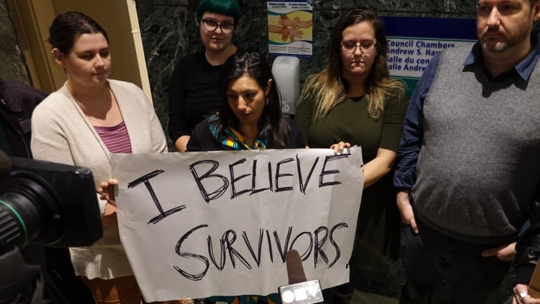 A group of people stands with a sign reading 'I believe survivors.'