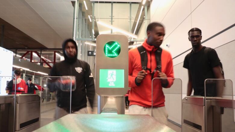 Several people approach a fare gate at an underground transit station.