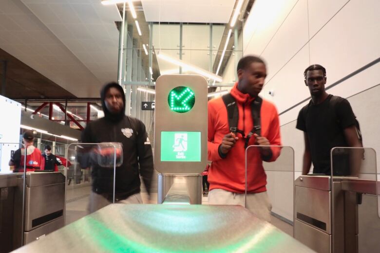 Several people approach a fare gate at an underground transit station.