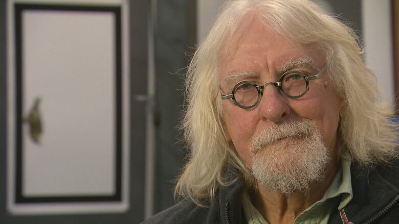 A man with shoulder-length blonde hair and small circular glasses.