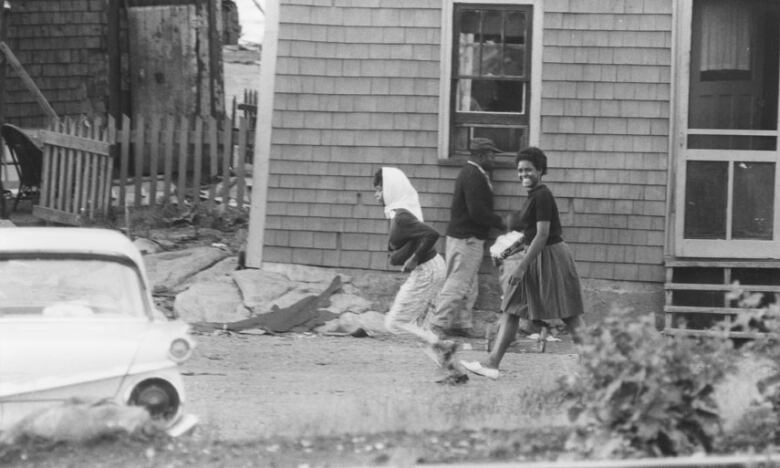 In an old black-and-white photograph, people are seen near a house in Africville.