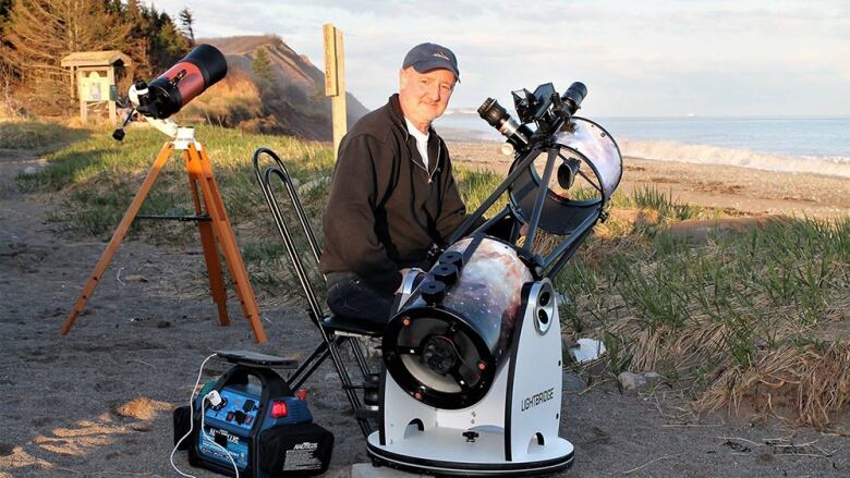 A man is shown by a beach with a large telescope.