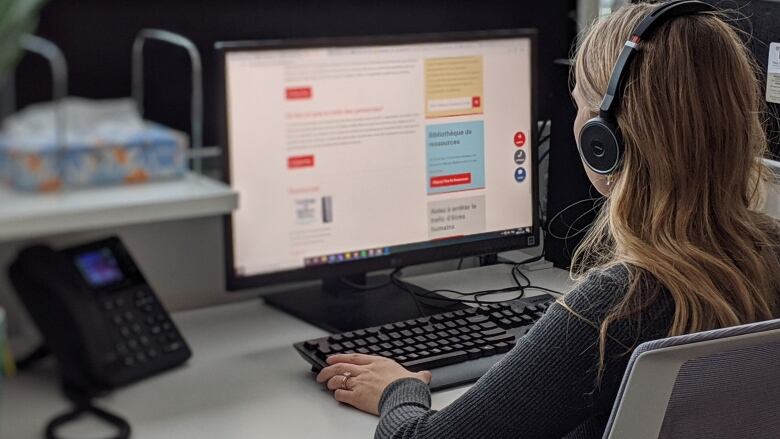 A woman typing at a computer with headphones on. 