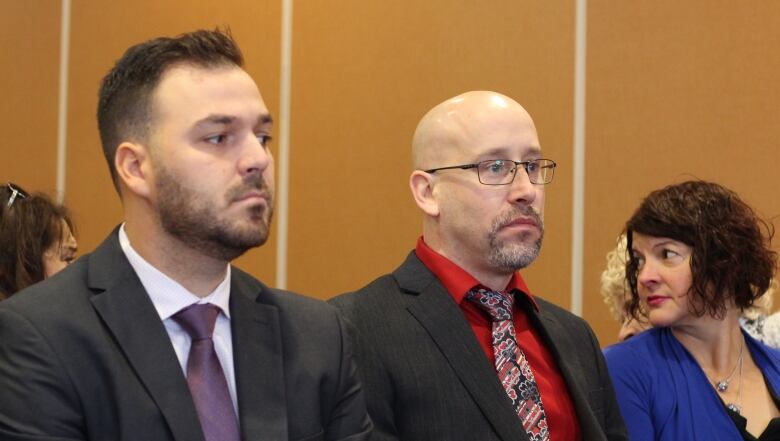 Two men looking ahead wearing suits.