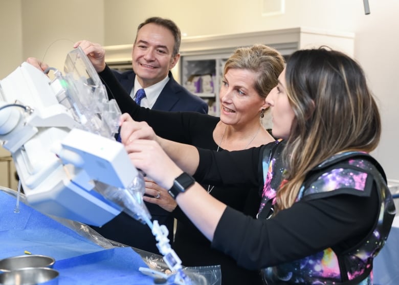 Three people look at medical equipment.