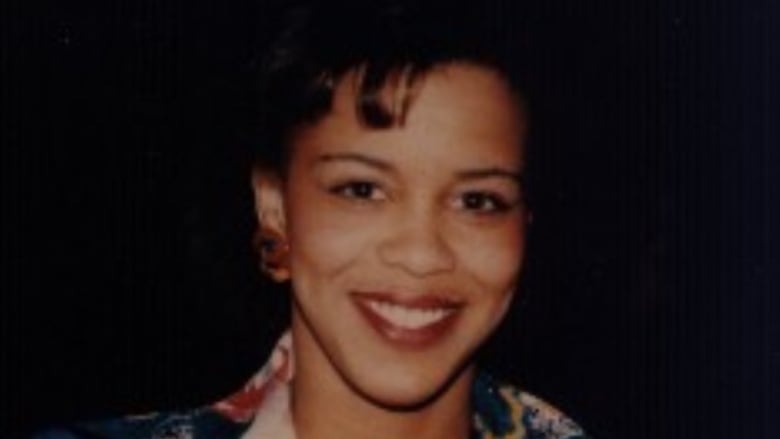 A Black woman smiling wearing red lipstick and a patterned top.