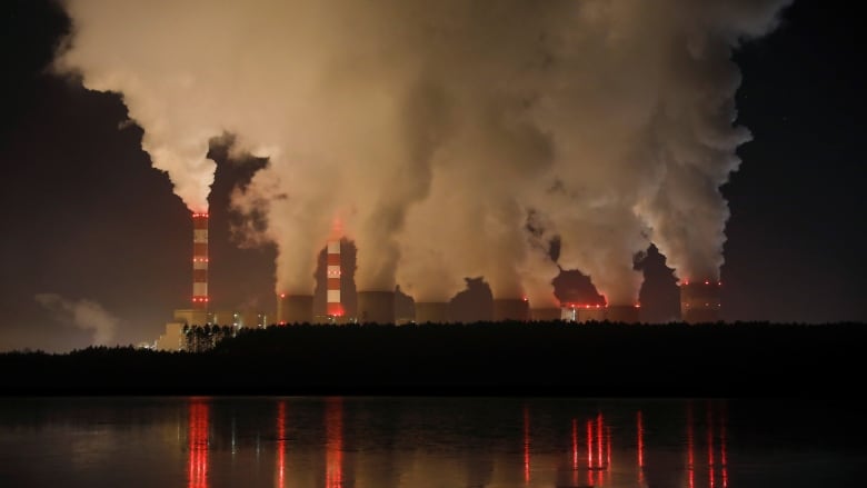 Far shot of smoke spewing out of a power plant's smoke stacks, viewed from across a lake or river.