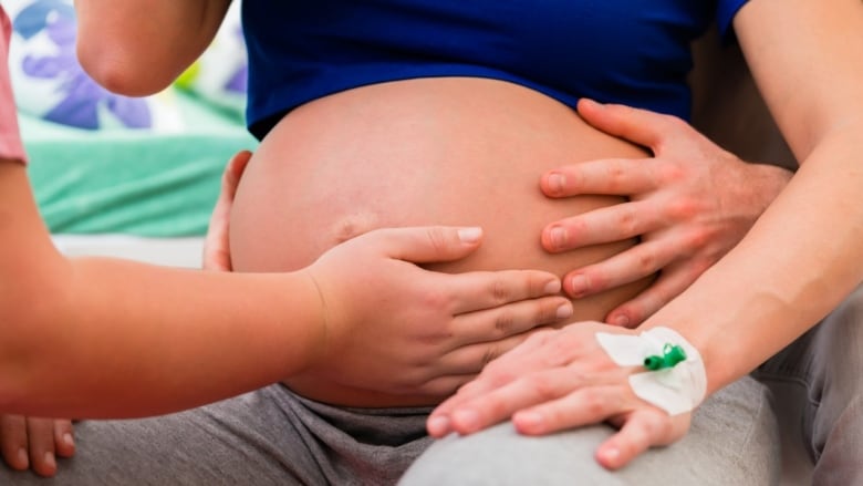 A woman places her hand on the pregnant belly of an expectant mother. 