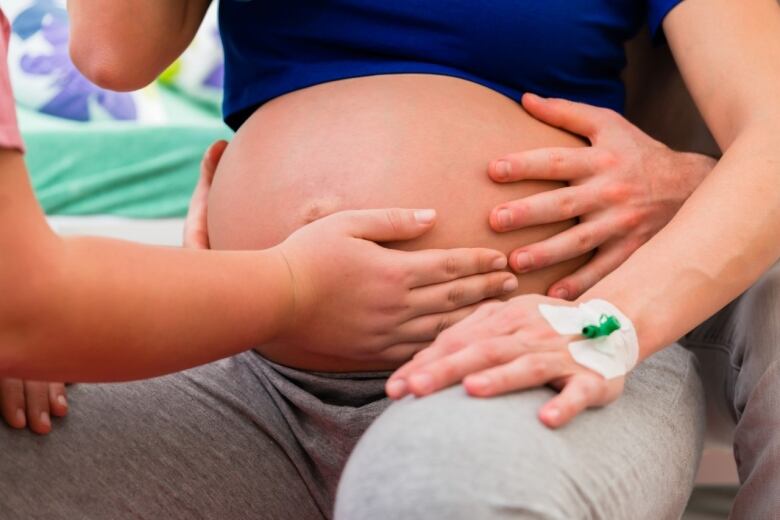 A woman places her hand on the pregnant belly of an expectant mother. 