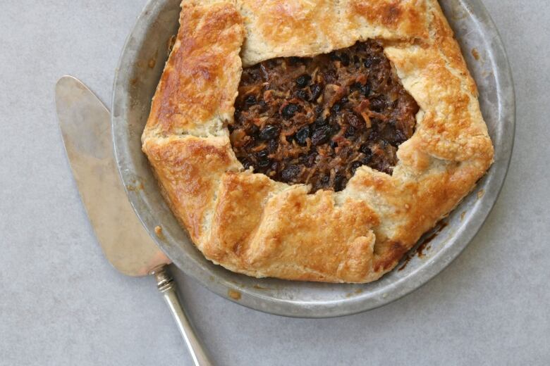 A butter knife lies next to a platter of mincemeat pie.  