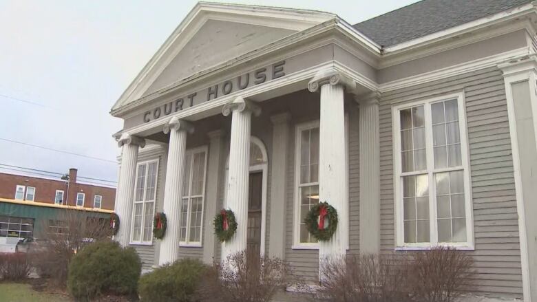 A grey and white building with the courthouse's name on the front is seen, with four white columns featured in the front. Holiday wreaths are hanging from the columns