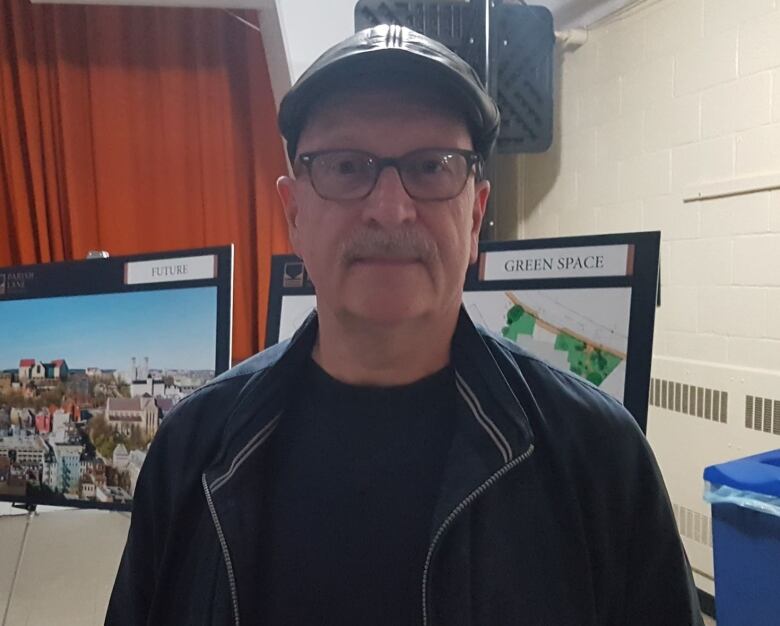 A man with a cap and jacket stands in a parish hall. 