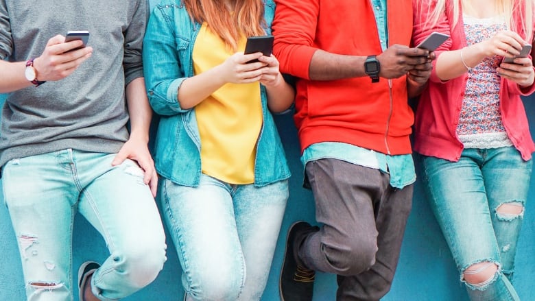 A number of youth leaning against a wall, all on their cell phones.