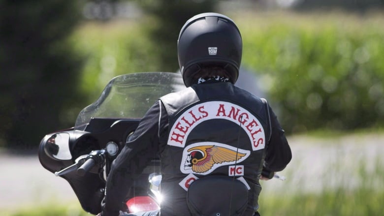 A person in a Hells Angels leather jacket rides a motorcycle 