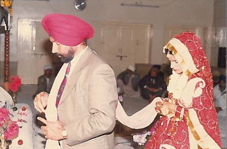 An old photo of a Sikh wedding shows a man in a turban walking with a woman holding fabric following behind him.