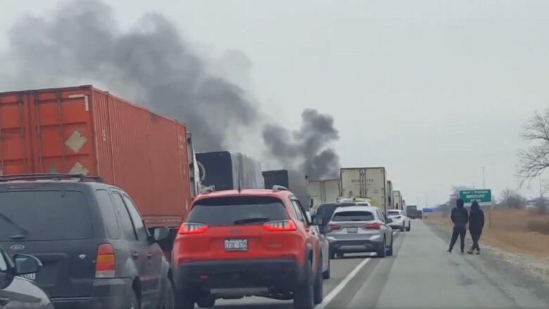 Cars in bumper-to-bumper traffic with some smoke in the distance.