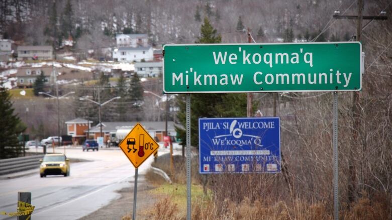 Image looking down the highway with a sign in the foreground saying, 'We'koqma'q Mi'kmaw Community.'