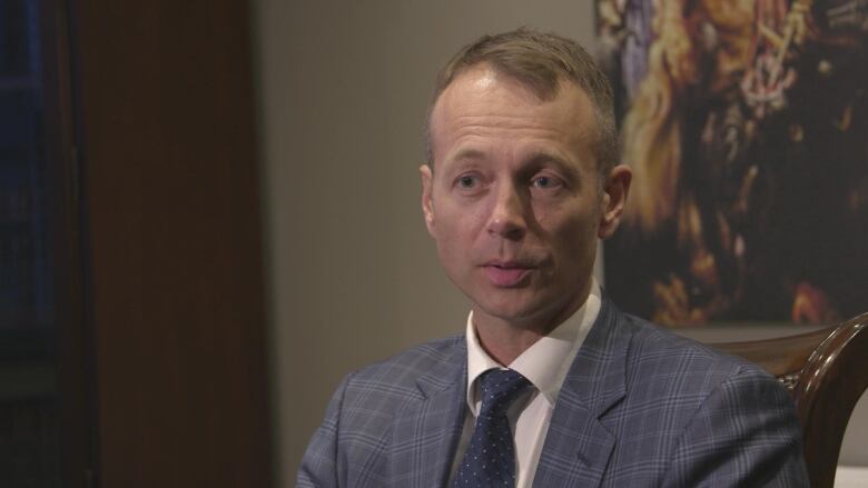 A man in a suit sits.