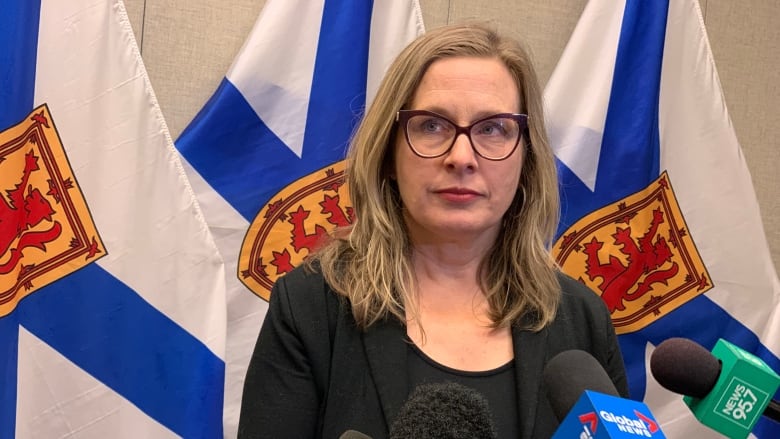 A woman in a black outfit looks at the camera in front of Nova Scotia flags. 