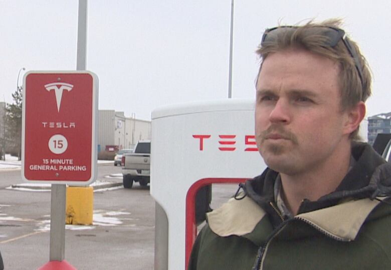 A man stands in front of a Tesla charging station.