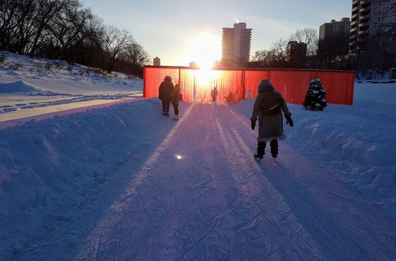 The sun sets as people skate on a frozen river