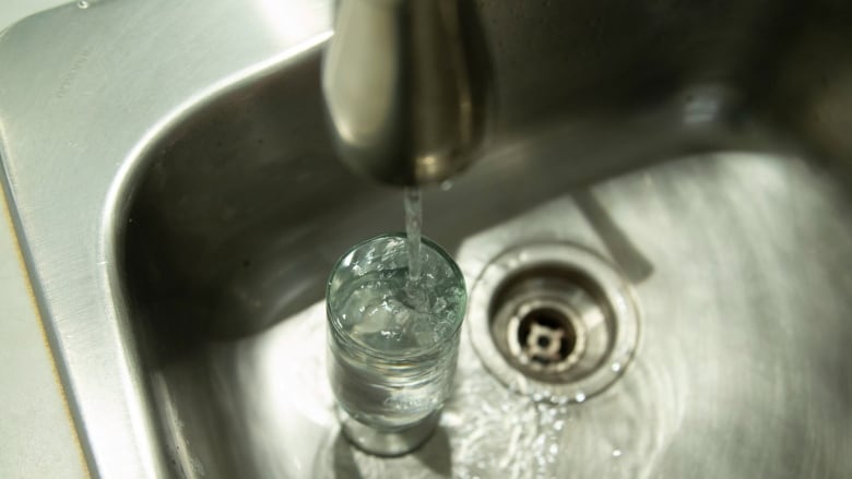 Tap water pours into a glass resting in a kitchen sink.