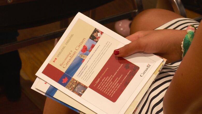 A woman holds booklets that say 'Becoming a Canadian Citizen.'