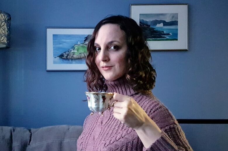 A woman hoists a tea cup while standing in a living room