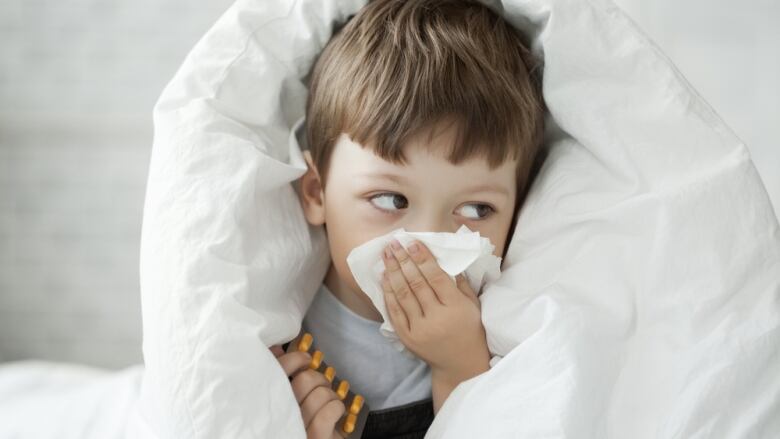 A sick child with a cold wipes his nose with a tissue.