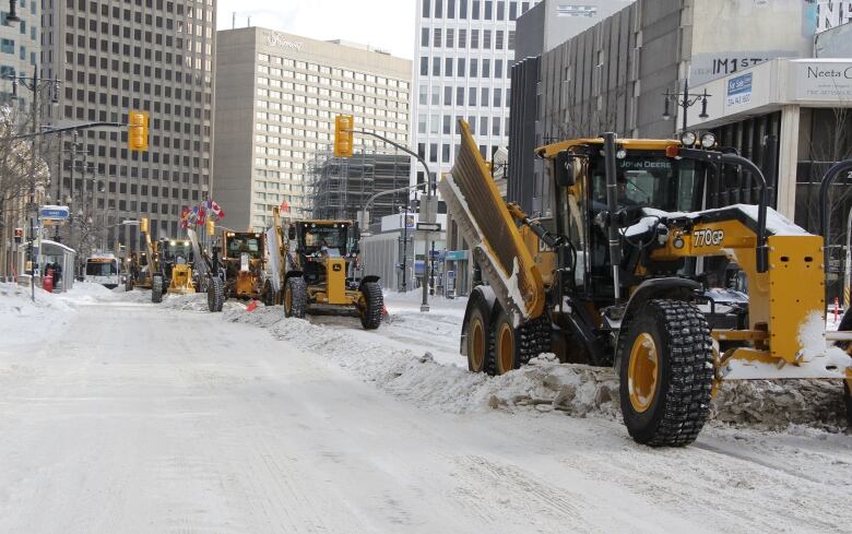 Several snow plows can be seen clearing a street. 