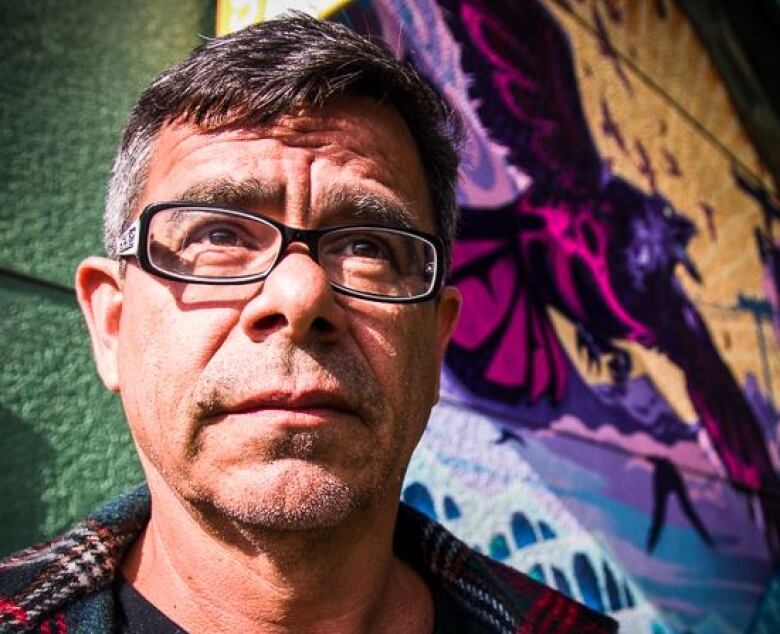 Portrait of an Indigenous man with short grey-black hair, in front of a colourful mural.