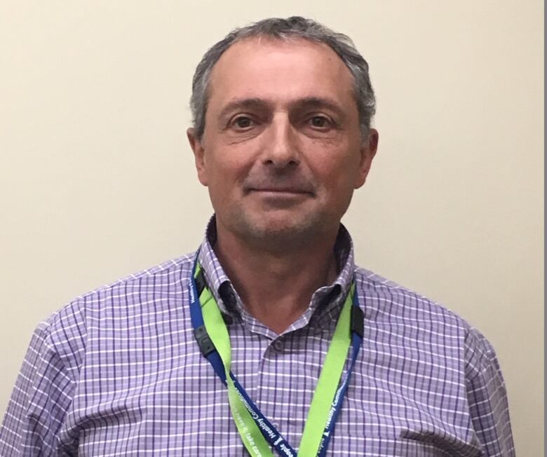 A man with grey hair is wearing a collared shirt layered with lanyards. 