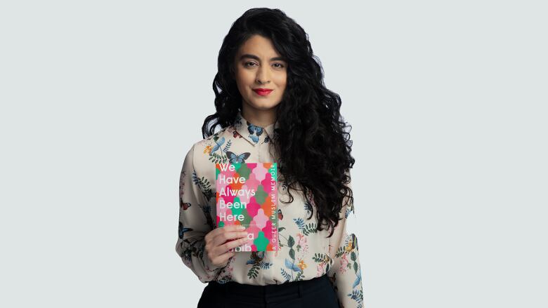 A woman with long dark hair and pink lipstick holding a book that matches her lip colour.