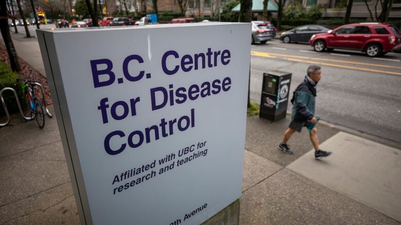 A sign indicating BC Centre for Disease Control in the pavement with a person walking by in the background