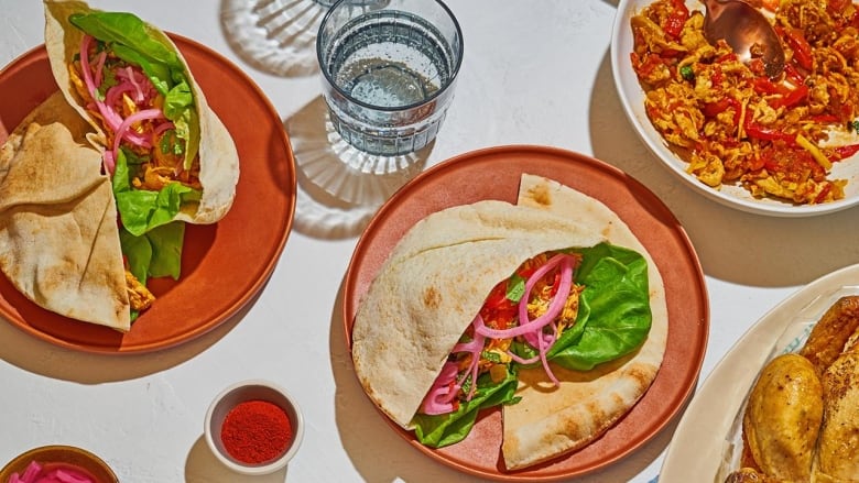 Overhead shot of 2 pink plates with stuffed pitas on them. The pitas are cut in half and filled with lettuce, chicken, and pickled onions. 