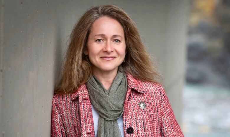 A woman with long brown hair in a scarf and pink-check jacket.