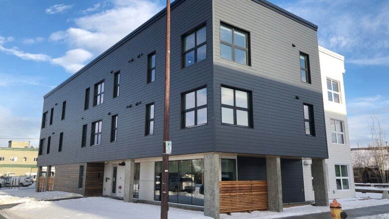 A rectangular grey 3-storey building sits on a corner lot, on a snowy day.