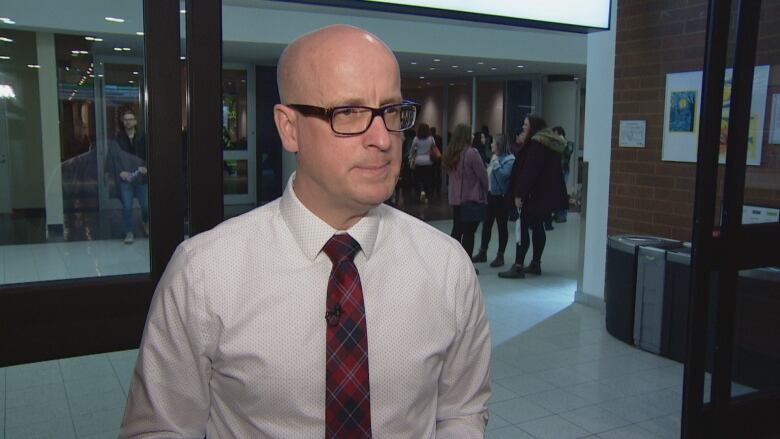 Jason Schilling is pictured during an interview standing in the hallway of a convention centre wearing a grey shirt, red tie and black glasses.