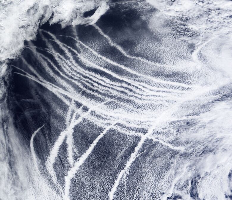 A satellite image shows clouds and what look like contrails in near parallel lines above a dark-blue ocean.