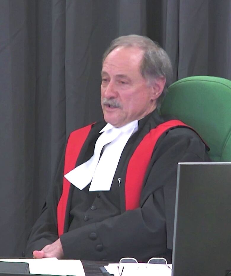 Judge wearing robes is seen presiding over an inquiry.